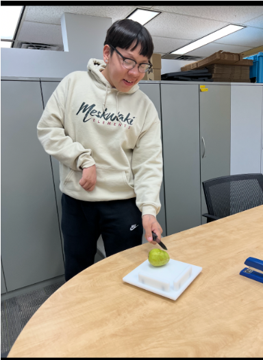 Desmond, a male student with short black hair and glasses, cutting a pear on a cutting board.