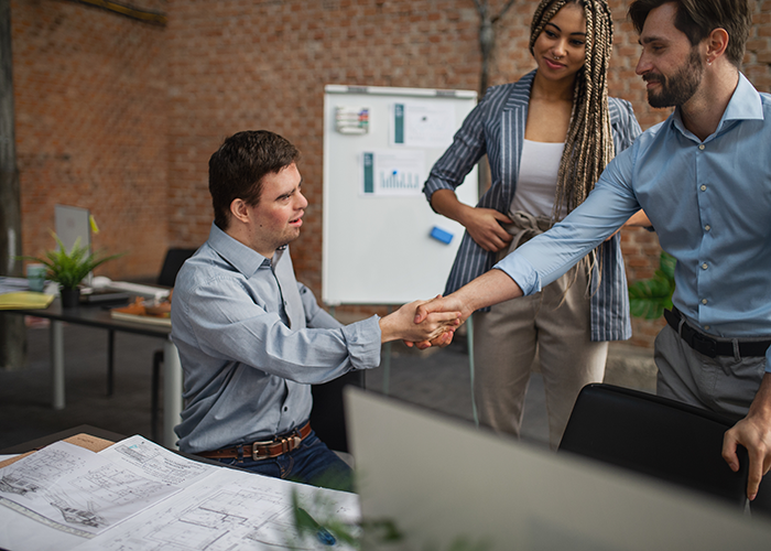 A man sitting at a desk and shaking the hand of another man