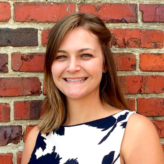 Photo of a white women with brown hair in front of a brick background.
