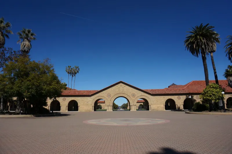 Woman with disability stands in cap and gown in front of campus clock tower building