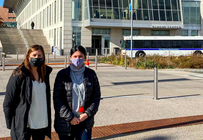 Two women, Ashley an Tatiana, stand in front of the UMass Boston Campus Center