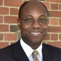 Image of Dr. Daniel A. Wubah, a Black man smiling wearing round glasses, a dark suit, and a shirt and tie.
