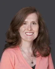 image of Irina Cain, a white woman with reddish brown long hair, smiling at the camera, wearing a peach colored sweater