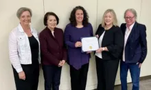 A person in purple shirt holding a certificate standing in the middle of four professionals