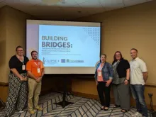 Two people stand to the left of a screen and three people stand to the right. On the screen a slide is projected that says “Building Bridges: The Growth of Regional Alliances in Advancing Inclusive Postsecondary Education” along with the GLIPSEA & ICI Think College logos