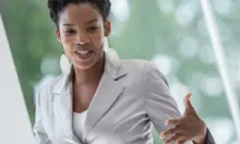 Woman of color in short sleeve blazer talking with her hands at front of a classroom
