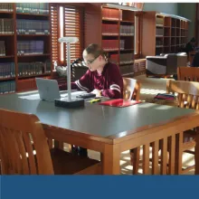 Girl leaning over books at a table in a library