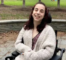 student smiling wearing a white sweater and sitting in a wheelchair