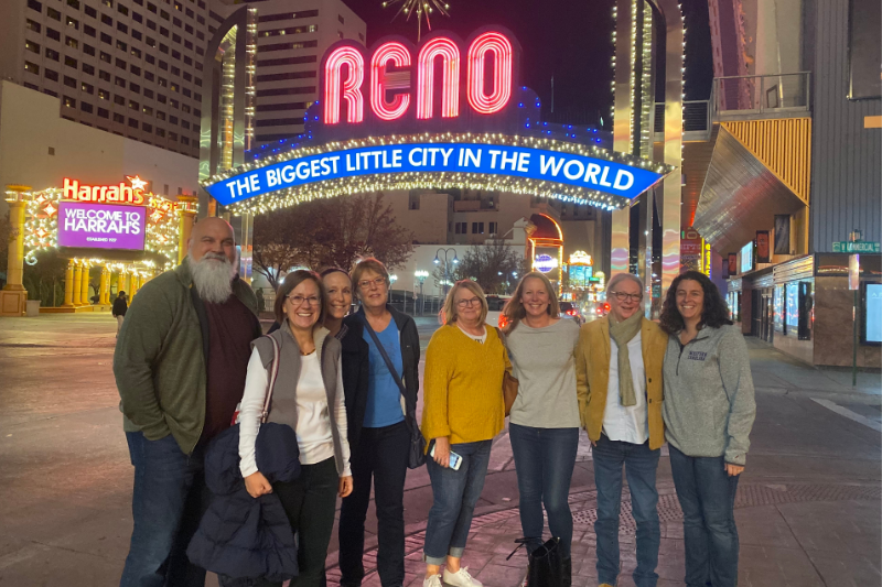 Group of people standing, smiling, in front of Reno: The Biggest Little City in the World sign