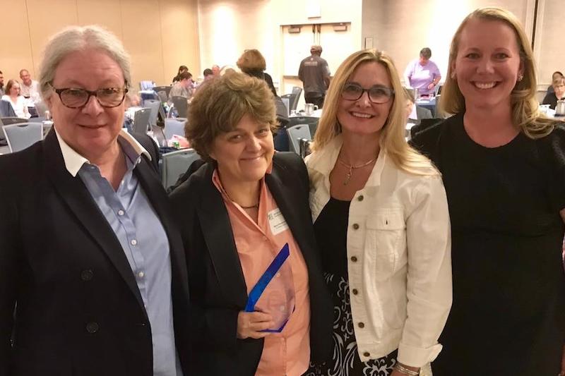 Four women standing together, smiling at the camera