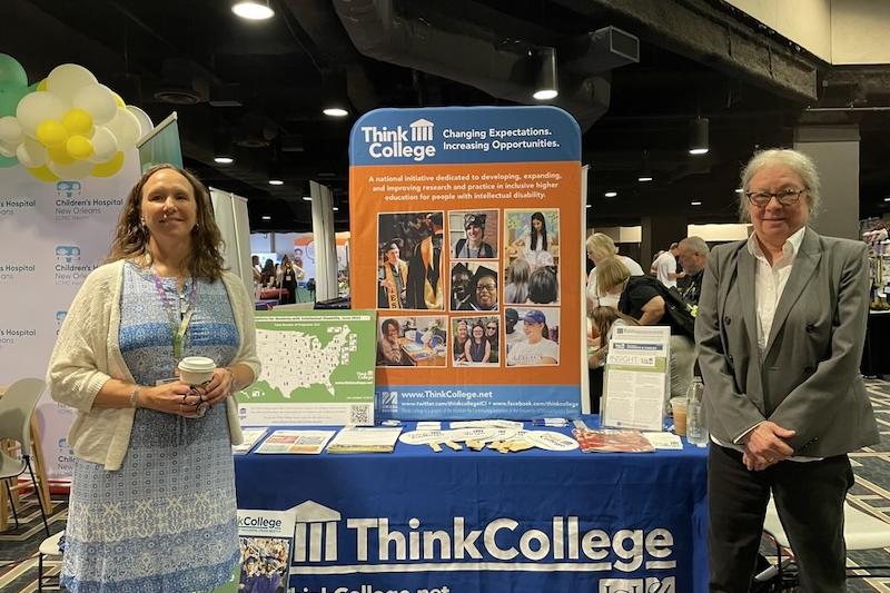 Two women stand at a Think College exhibit table at a conference