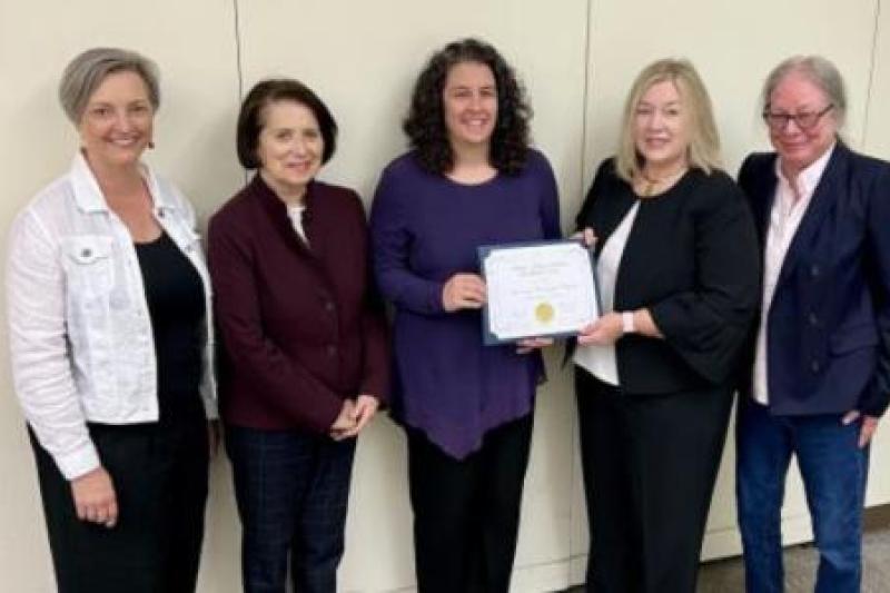 Five women standing together, with Kelly Kelley in the center, wearing purple, holding a certificate of accreditation