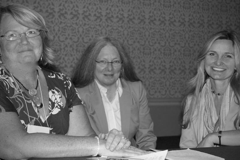 Black & white photo of three women sitting together smiling at the camera