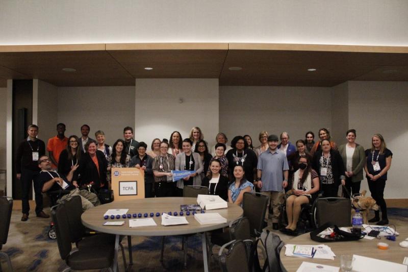 Photograph of 32 people posed in a meeting room, holding a sign that says TCPA.