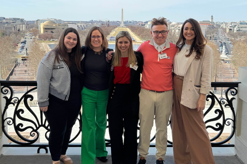 Five people stand together smiling atop the Speaker’s Balcony in the US Capitol building.