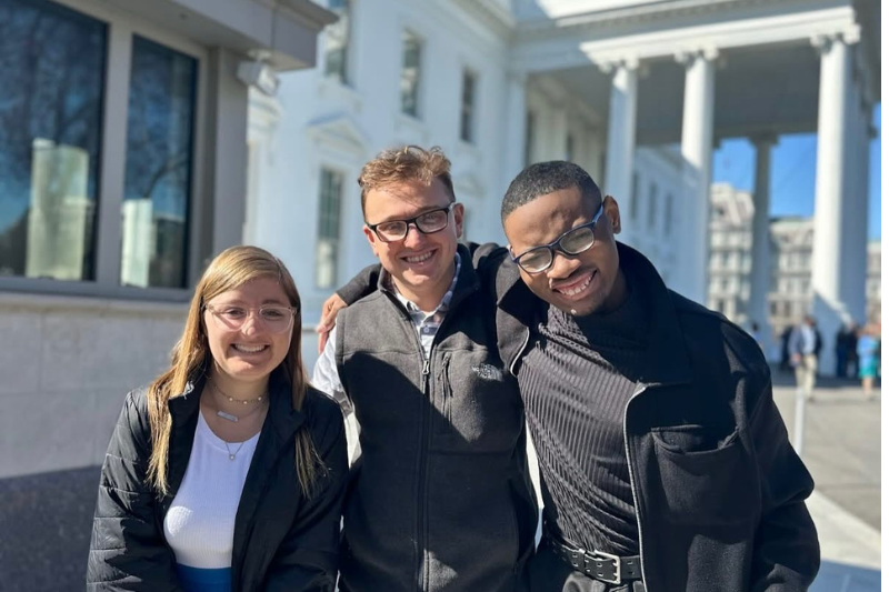 Three people smile for a photo outside of the White House.