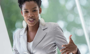 Woman of color in short sleeve blazer talking with her hands at front of a classroom