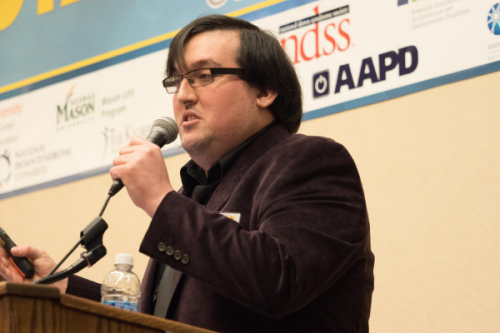 photo of Kenneth Kelty speaking at a conference.  he is holding a microphone and standing behind a lectern.