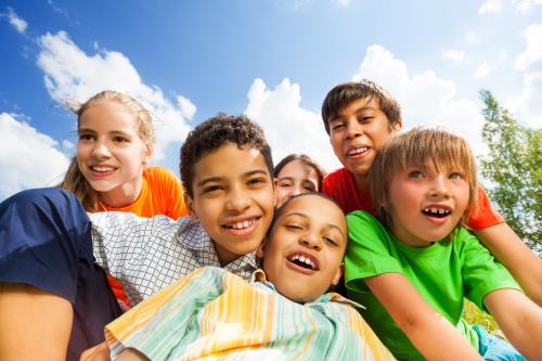 group of 6 elementary-aged kids crowded together, smiling, with blue sky in the background